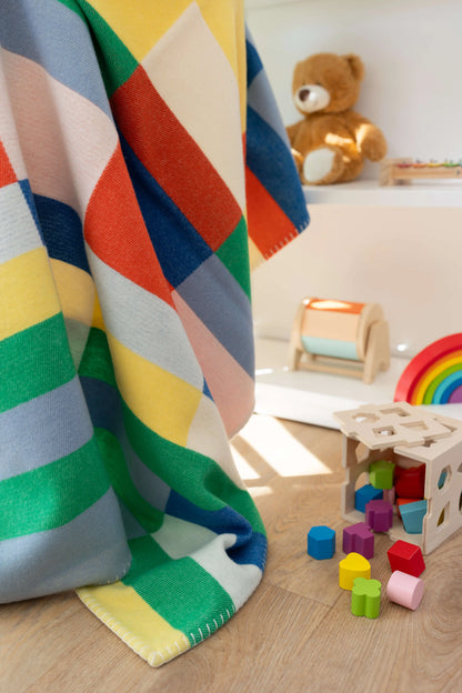 2025 Johnstons of Elgin Interiors Collection  Block Stripe' Children's Blanket draped over a chair in a children's playroom surrounded by  toys TB000582RU7439ONE