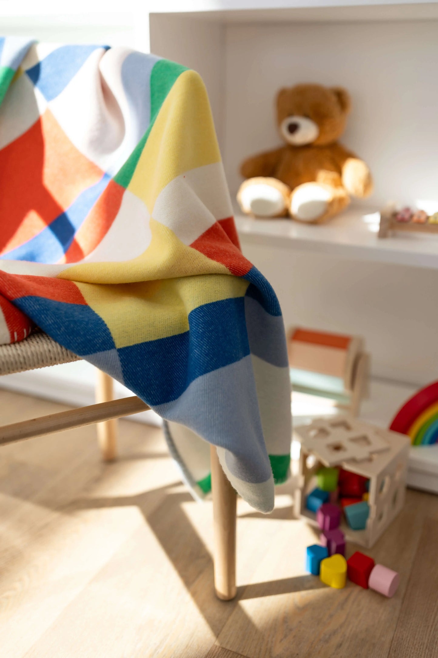 2025 Johnstons of Elgin Interiors Collection  Block Stripe' Children's Blanket draped over a chair in a children's playroom surrounded by teddy bears and toys TB000582RU7439ONE