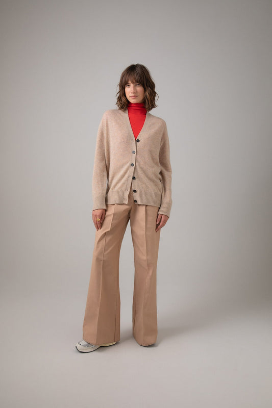Johnstons of Elgin Gauzy Cashmere Women's V Neck Cardigan in Oatmeal worn over a Red Roll Neck with Beige Wide Leg Trousers on a grey background KAA04991HB0210