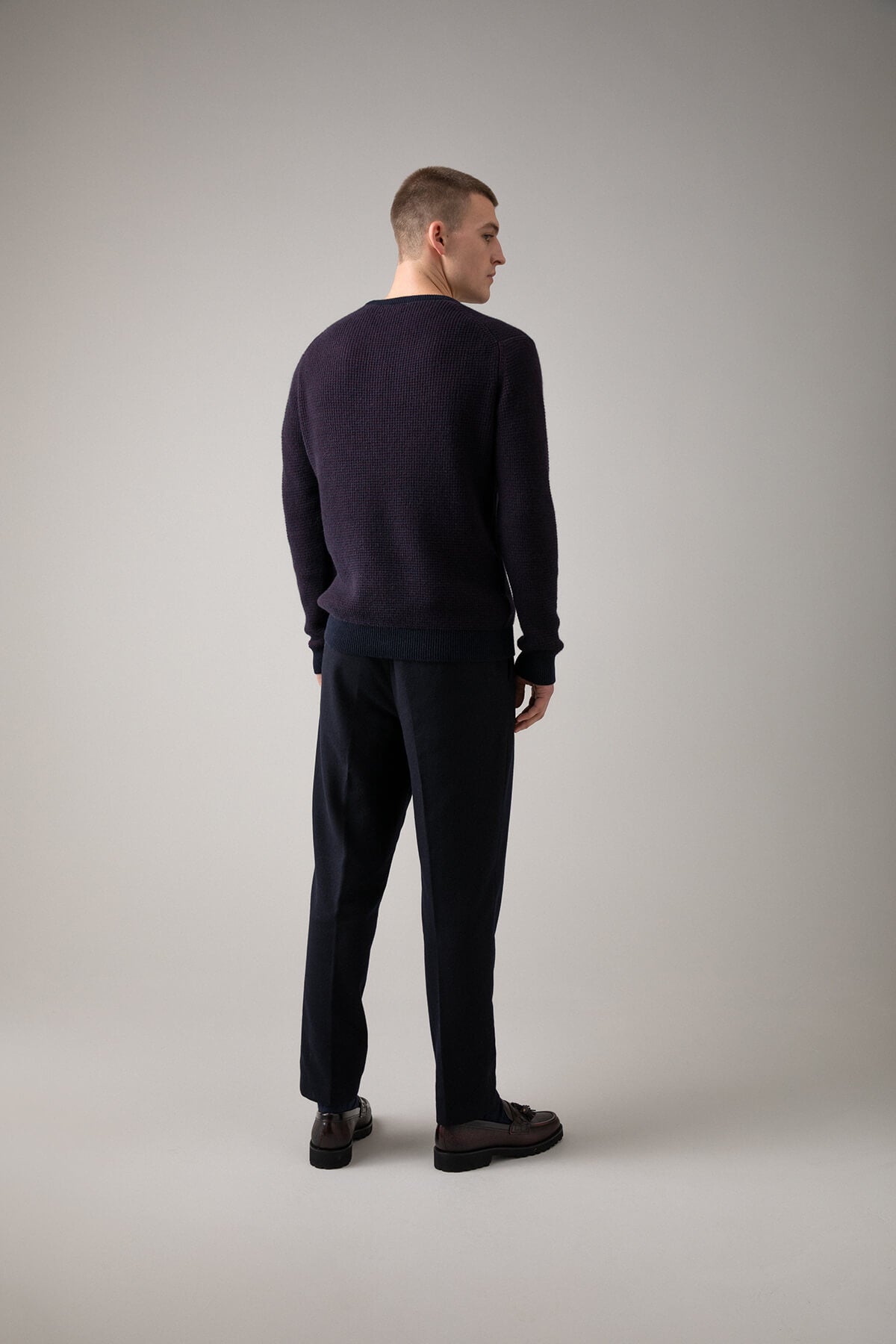 Johnstons of Elgin’s Men's Textured Waffle Rib Cashmere Jumper in Bramble on model wearing navy trousers on a grey background KAA05042Q23701
