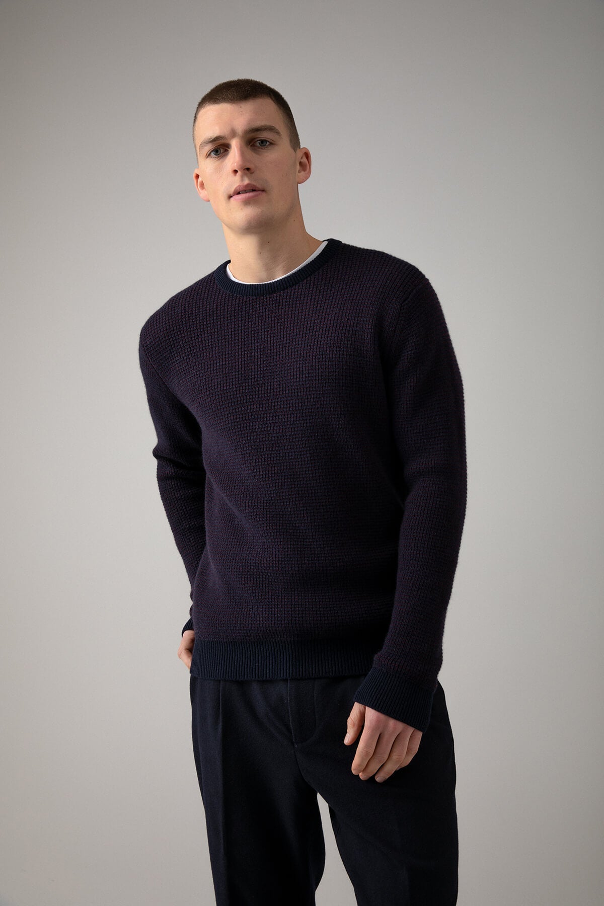 Johnstons of Elgin’s Men's Textured Waffle Rib Cashmere Jumper in Bramble on model wearing navy trousers on a grey background KAA05042Q23701