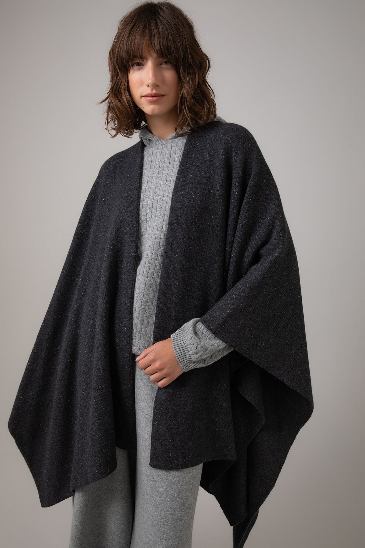 Johnstons of Elgin Double Face Donegal Cashmere Cape in Charcoal worn with Grey Cable Cashmere Hoodie on a grey background KAA05102Q23681ONE