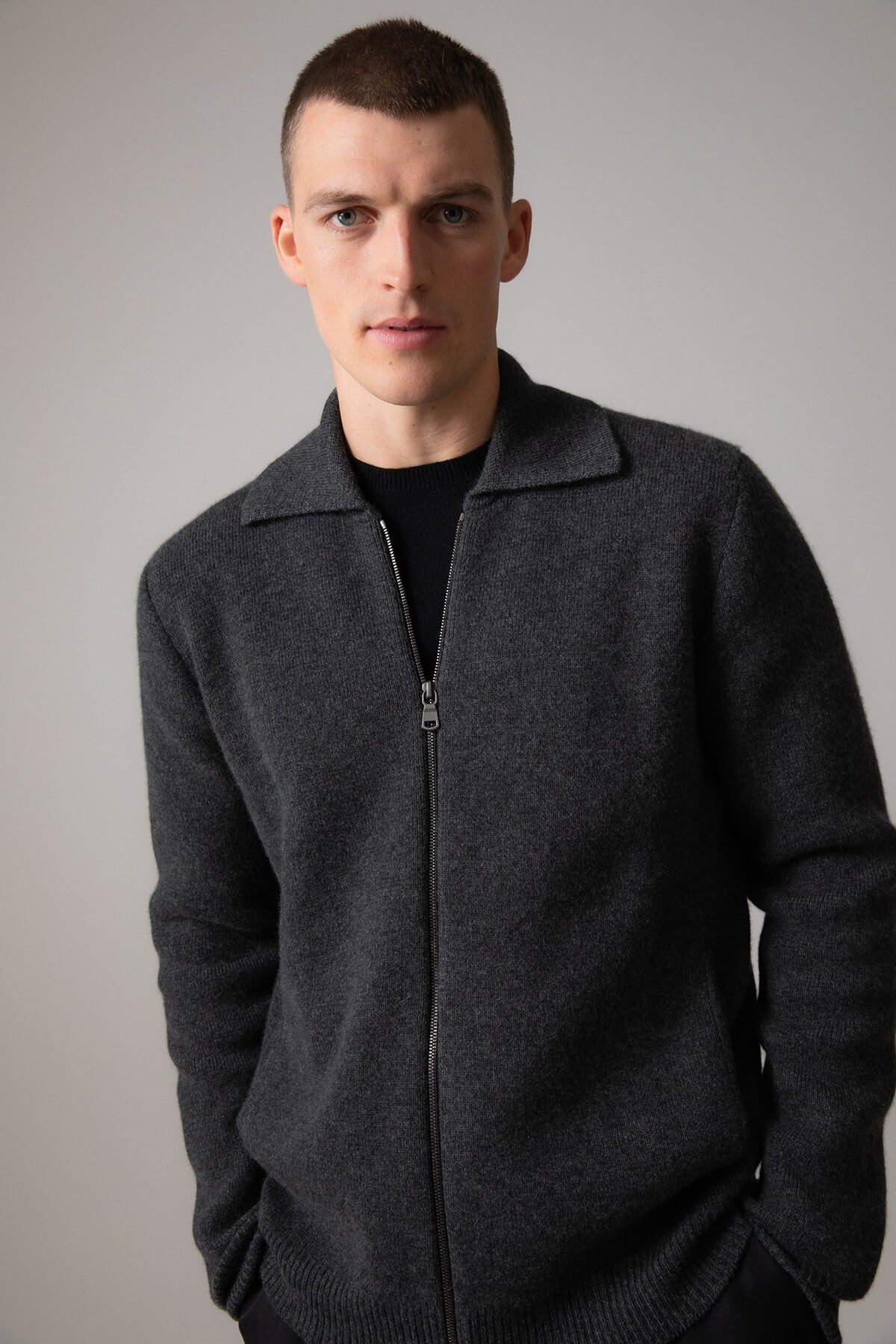 Johnstons of Elgin’s Men's Milano Stitch Cashmere Zip Jacket in Charcoal grey on model wearing black trousers on a grey background KAA05113HA7165