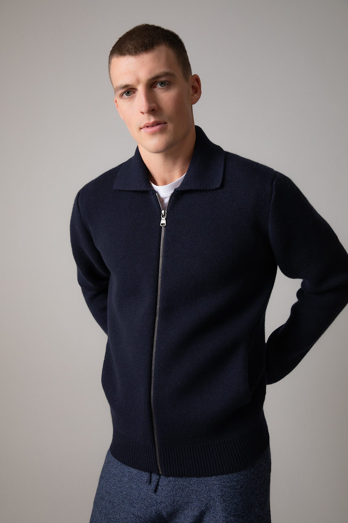 Johnstons of Elgin’s Men's Milano Stitch Cashmere Zip Jacket in Dark Navy on model wearing blue joggers on a grey background KAA05113SD7286