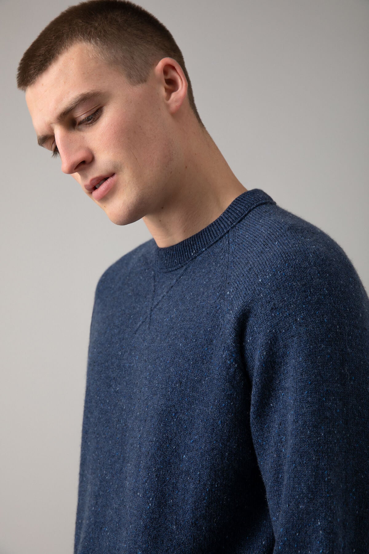 Johnstons of Elgin’s Men's Cashmere Donegal Sweatshirt in Denim blue on model on a grey background KAA05147004544