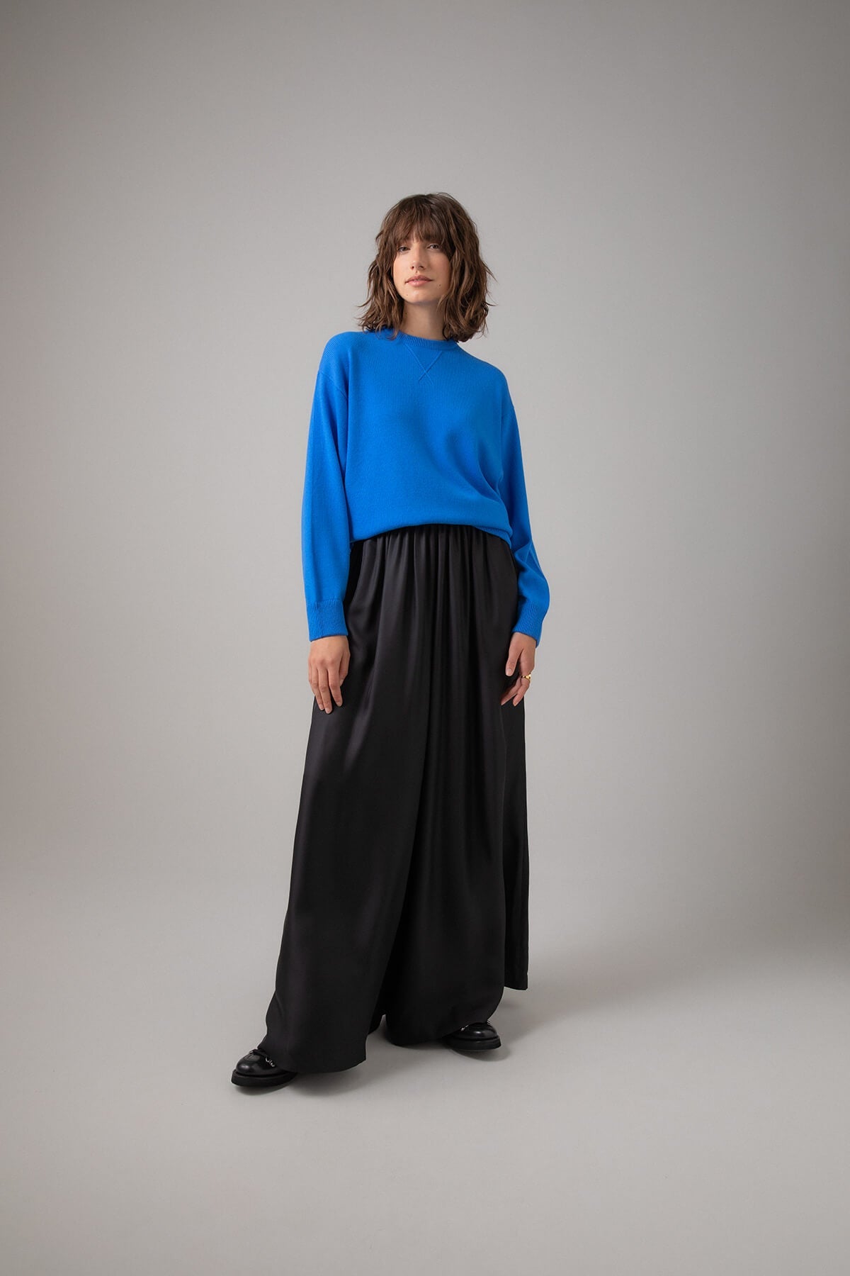 Johnstons of Elgin Women's Cashmere Girlfriend Style Sweatshirt in Orkney Blue worn with a Black Long Skirt on a grey background KAA05158SD4991