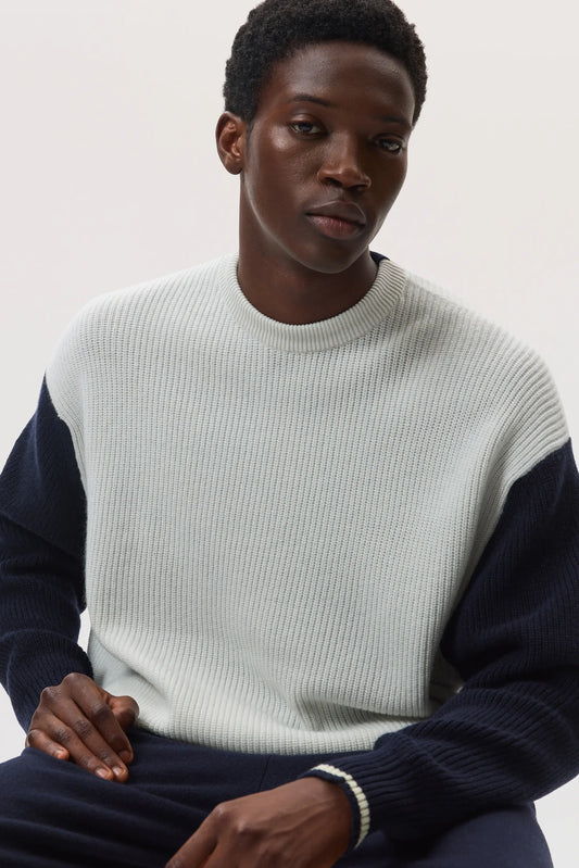 Model sitting down wearing Johnstons of Elgin SS25 Men's Knitwear Navy & White  Cashmere Colour Block Relaxed Rib Crew Neck Sweater with navy trousers on a white background KAA05412Q25138