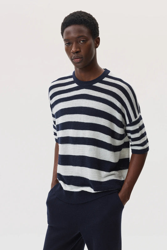 Male model wearing Johnstons of Elgin SS25 Unisex Knitwear Navy & White Textured Stripe Oversized Cashmere T-Shirt with navy trousers against a white backdrop KAA05414Q25123