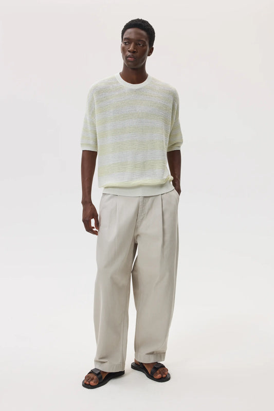 Male model wearing Johnstons of Elgin SS25 Unisex Knitwear White & Lemon Textured Stripe Oversized Cashmere T-Shirt with cream chino trousers and black sandals against a white backdrop  KAA05414Q25127