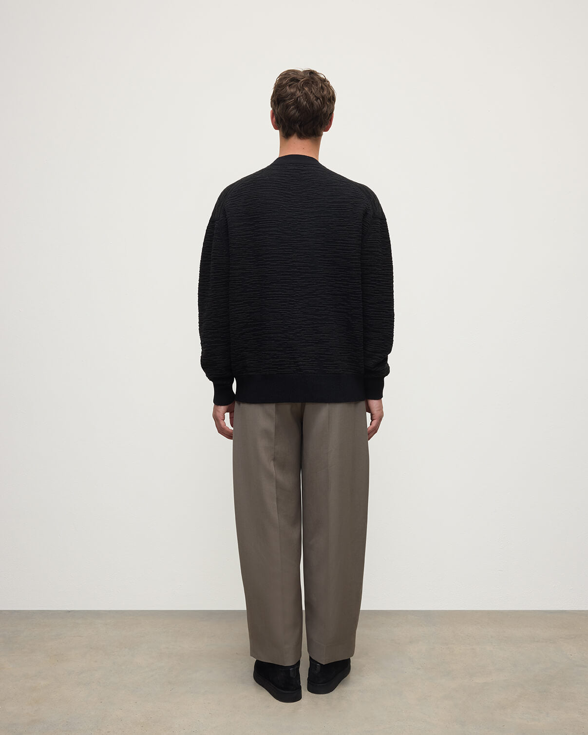 Model wearing Johnstons of Elgin AW25 Men's Knitwear Black & Iron Plaited Texture Black Cashmere Cardigan Back View KAA05579Q25387