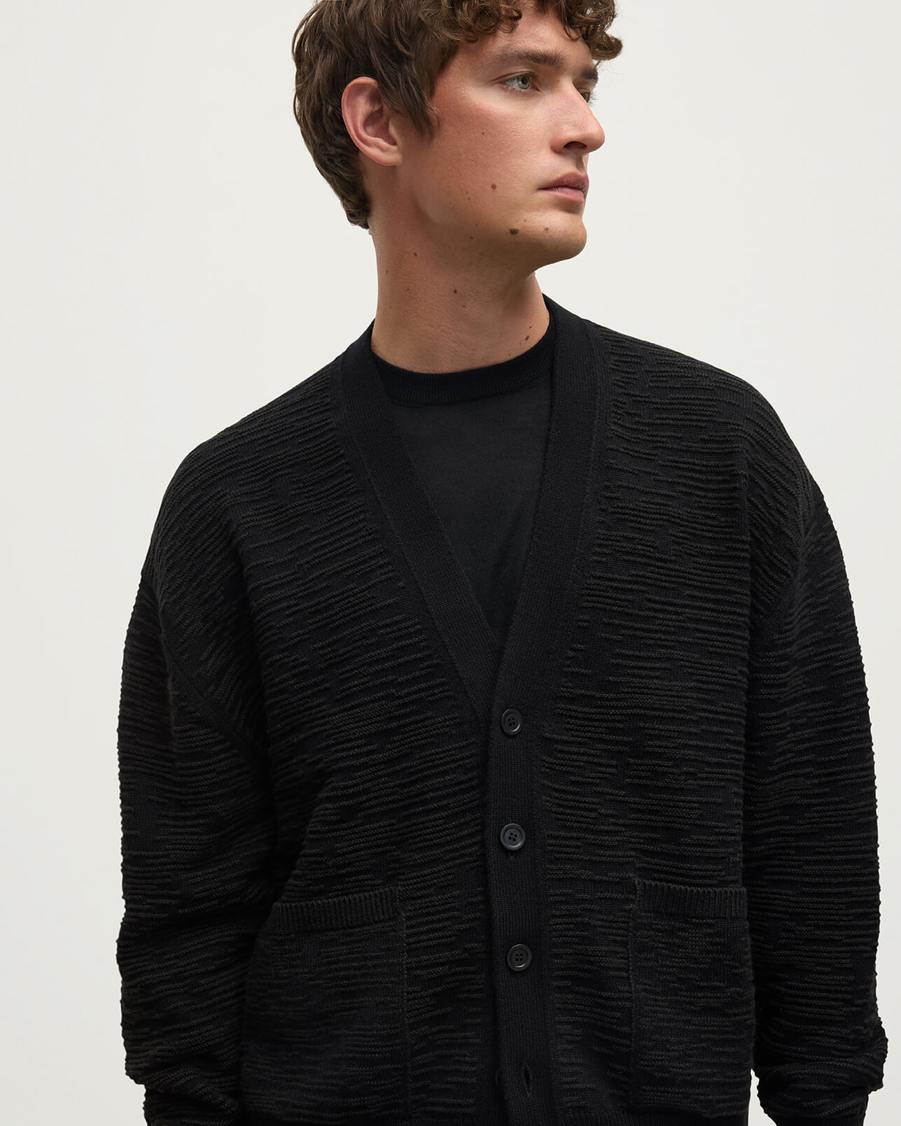 Model wearing Johnstons of Elgin AW25 Men's Knitwear Black & Iron Plaited Texture Black Cashmere Cardigan Close Up  KAA05579Q25387