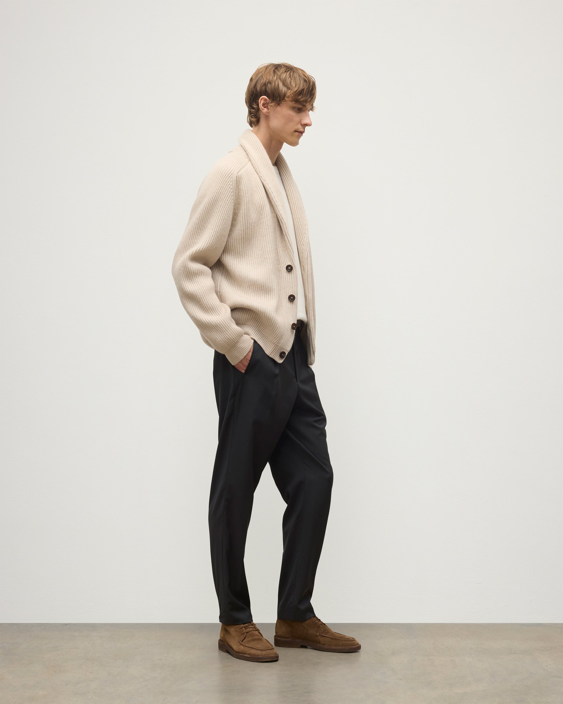 MALE MODEL WEARING JOHNSTONS OF ELGIN PIONEER SHAWL CARDIGAN NATURAL 100% CASHMERE OVER A CREAM CASHMERE SWEATER WITH GREY TROUSERS AND BROWN SUEDE LOAFERS KAA05750Q26191
