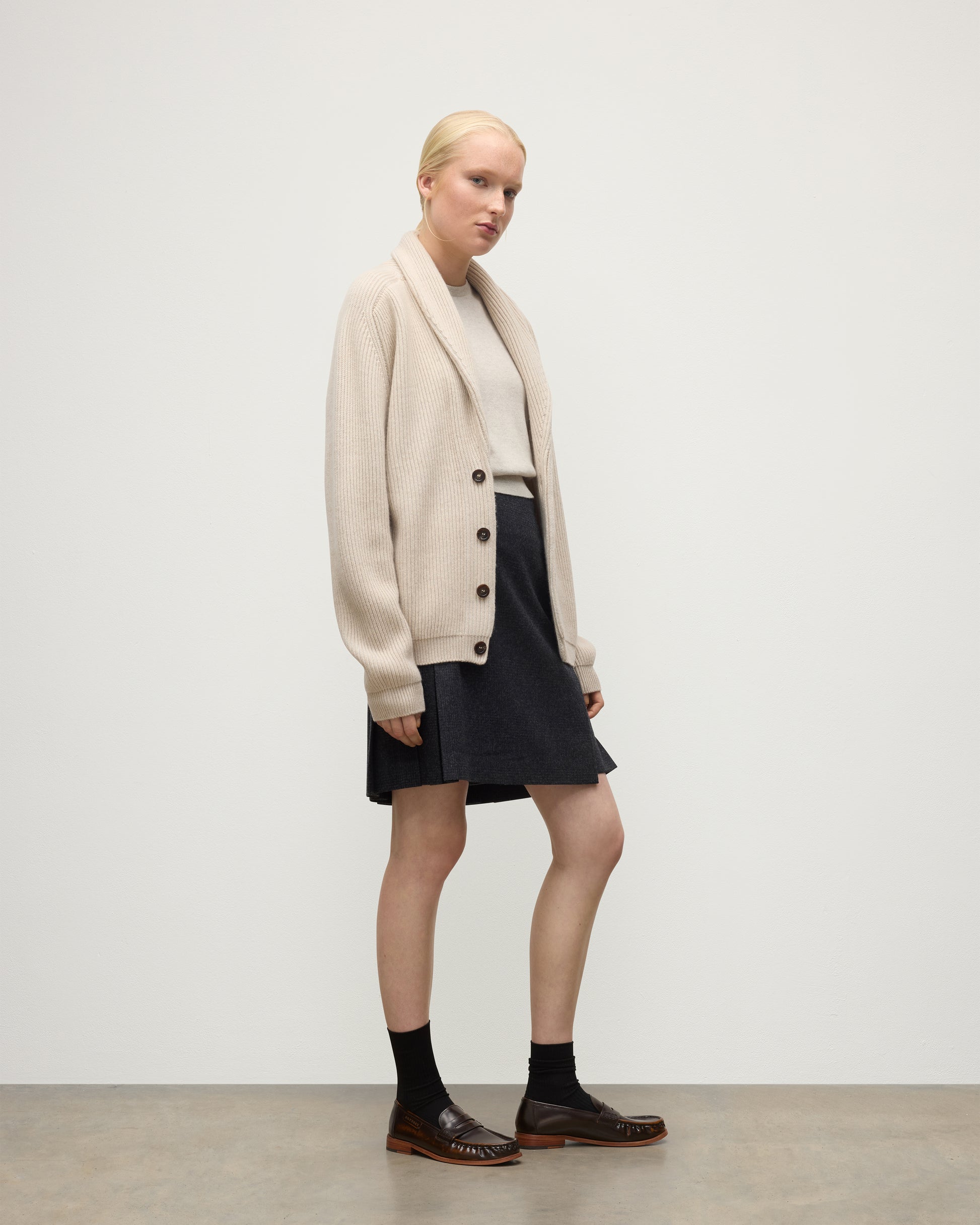 FEMALE MODEL WEARING JOHNSTONS O F ELGIN PIONEER SHAWL CARDIGAN NATURAL 100% CASHMERE WITH MATCHING CASHMERE SWEATER AND CHARCOAL SHORT LE KILT SKIRT & LOAFERS UAA05750Q26191