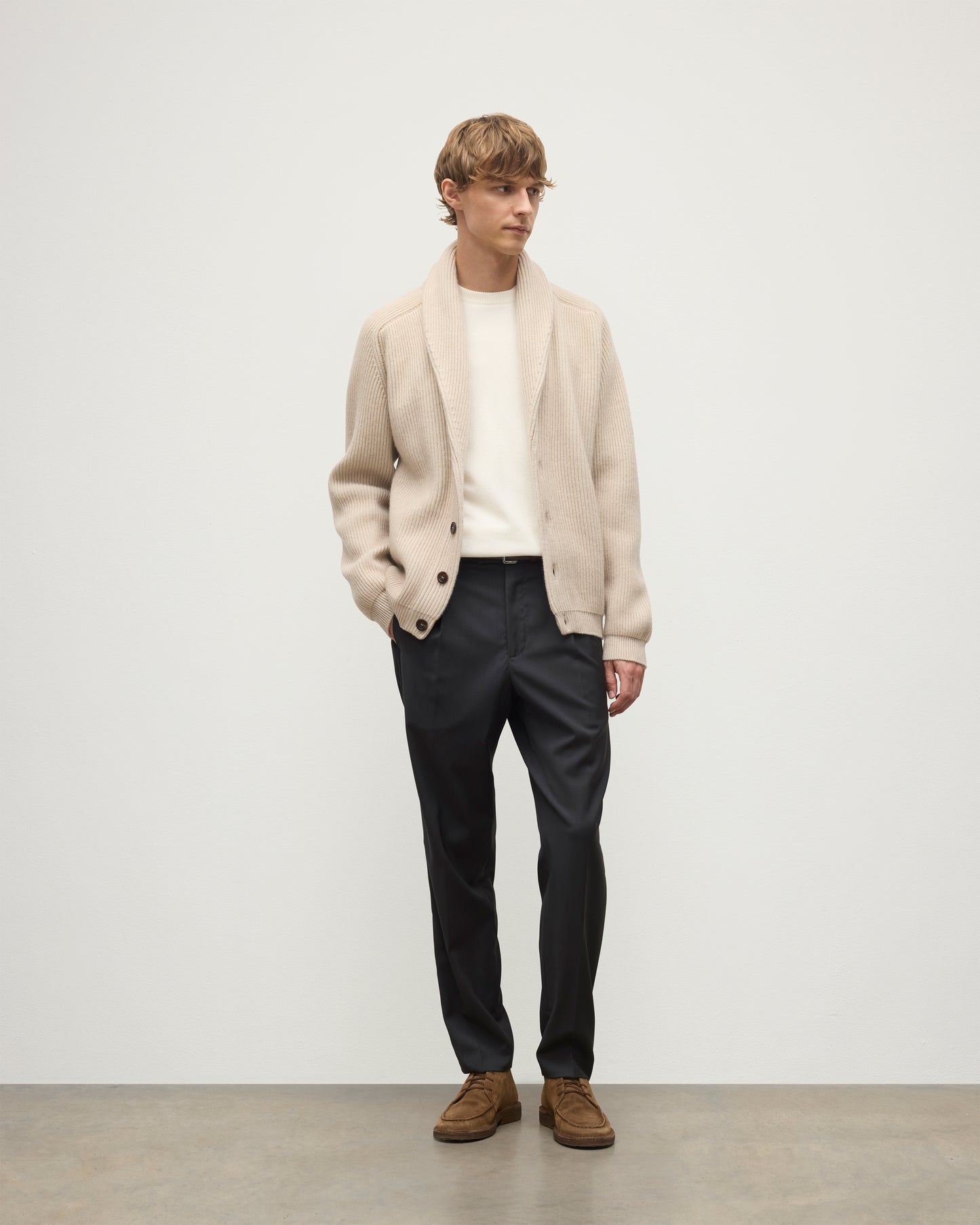 MALE MODEL WEARING JOHNSTONS OF ELGIN PIONEER SHAWL CARDIGAN NATURAL 100% CASHMERE OVER A CREAM CASHMERE SWEATER WITH GREY TROUSERS AND BROWN SUEDE LOAFERS KAA05750Q26191