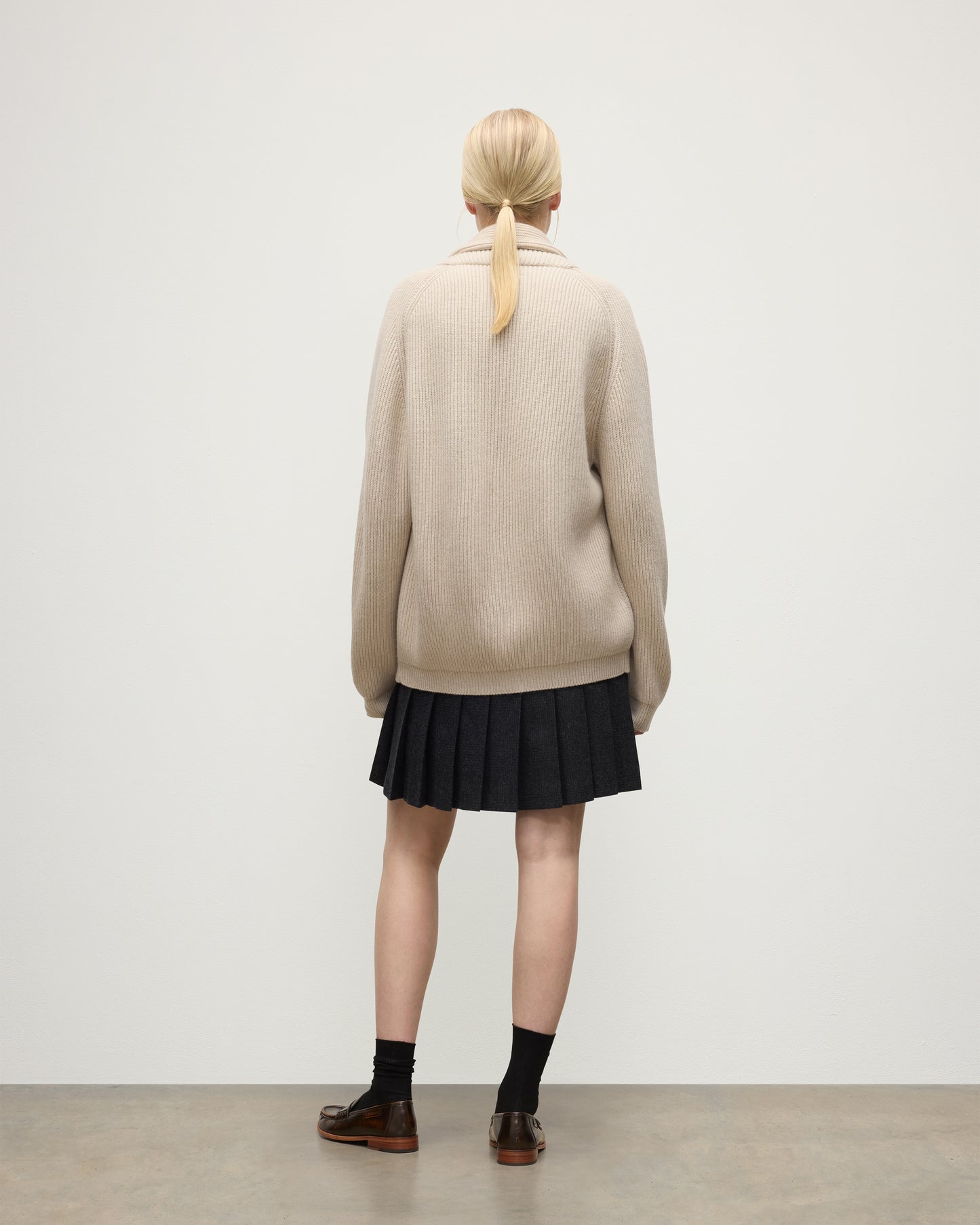 BACK OF FEMALE MODEL WEARING JOHNSTONS O F ELGIN PIONEER SHAWL CARDIGAN NATURAL 100% CASHMERE WITH MATCHING CASHMERE SWEATER AND CHARCOAL SHORT LE KILT SKIRT & LOAFERS UAA05750Q26191