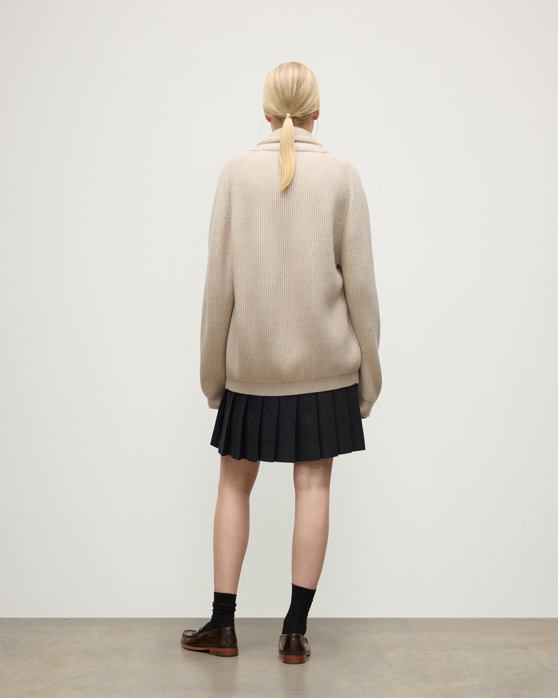 BACK OF FEMALE MODEL WEARING JOHNSTONS O F ELGIN PIONEER SHAWL CARDIGAN NATURAL 100% CASHMERE WITH MATCHING CASHMERE SWEATER AND CHARCOAL SHORT LE KILT SKIRT & LOAFERS UAA05750Q26191