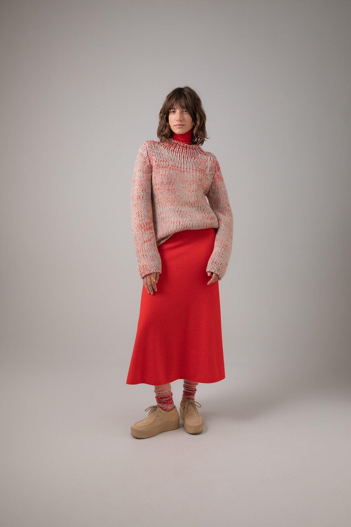 Johnstons of Elgin Women's A-Line Cashmere Skirt in Orkney Red worn with a Red Marl Cashmere Neck Sweater on a grey background KAP05097SE0661