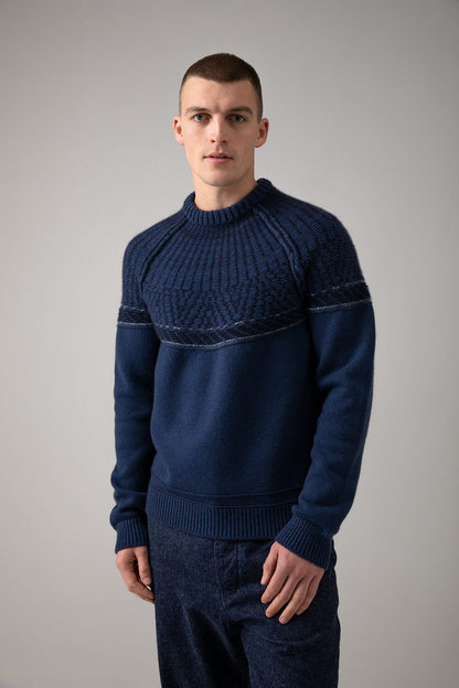 Johnstons of Elgin’s Men's Fairisle Yoke Cashmere Jumper in Ocean blue on model wearing blue trousers on a grey background KAB05108Q23716