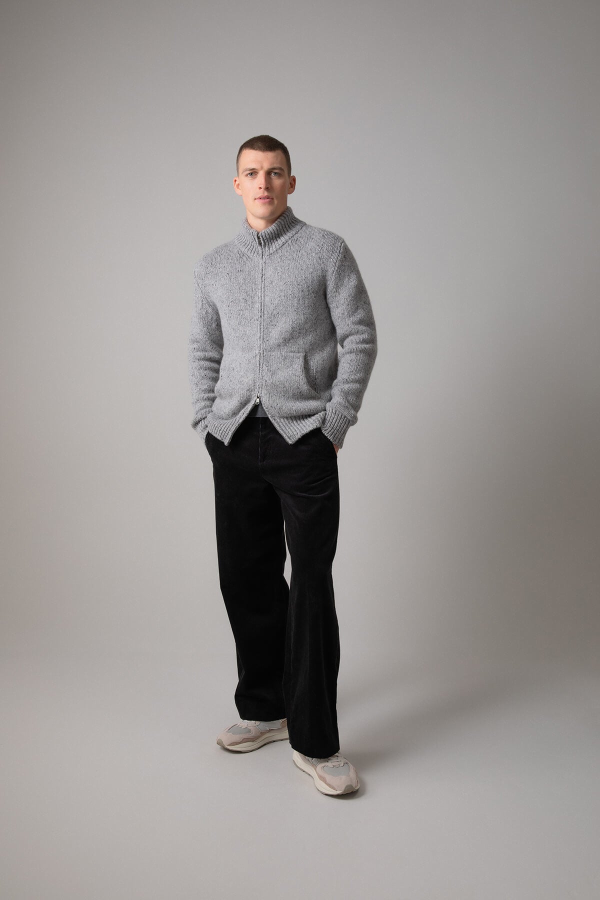 Johnstons of Elgin’s Men's Cashmere Donegal Zip Turtle Neck Cardigan in Light Grey on model wearing black trousers on a grey background KAB05115Q23711