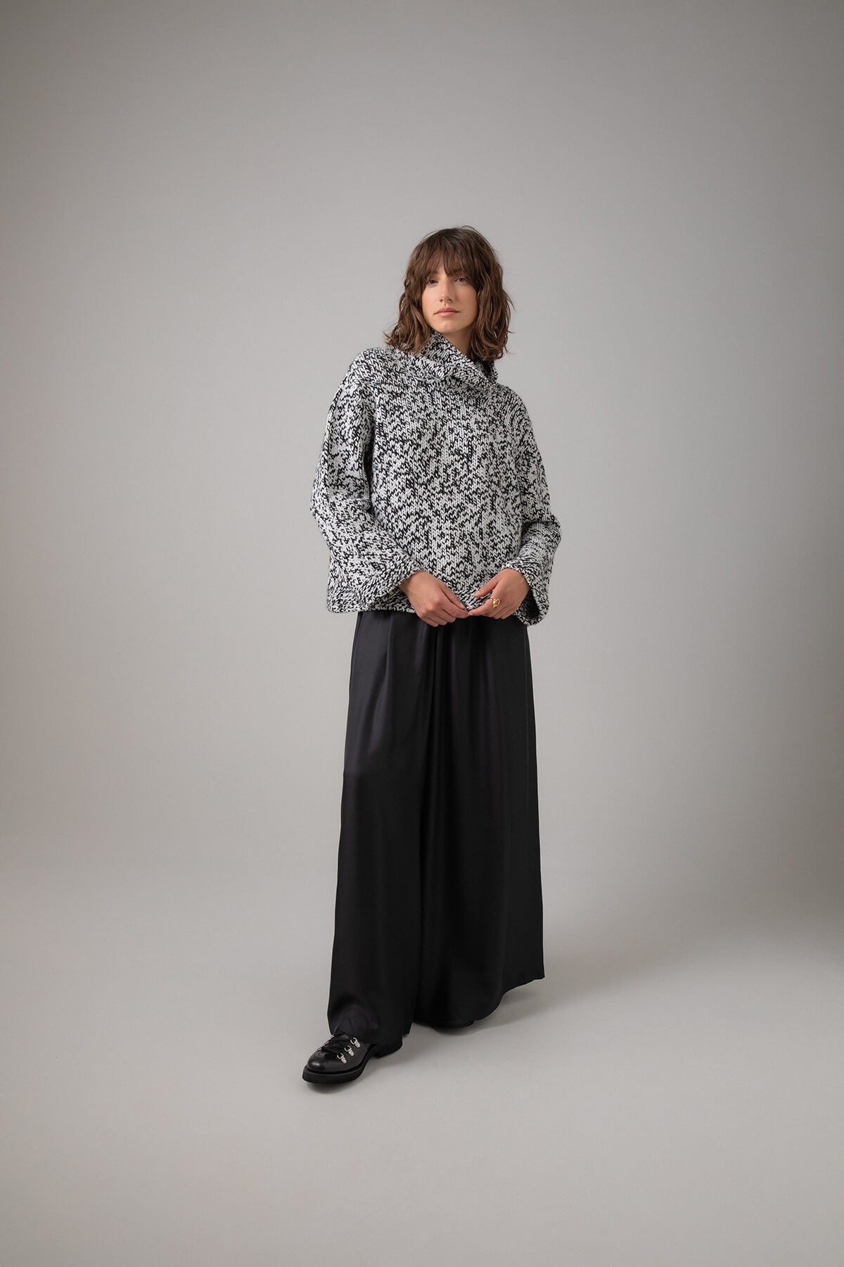 Johnstons of Elgin Women's Handknit Look Cashmere Marl Roll Neck Sweater in Black & White Marl worn with a Long Black Skirt on a grey background KAB05154HA7149