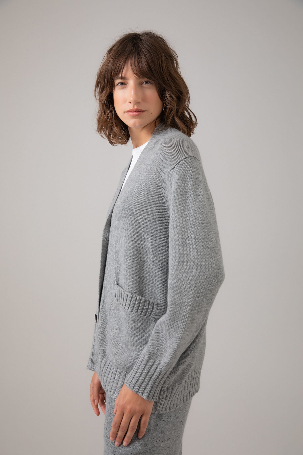 Side view of a Johnstons of Elgin Women's Relaxed Fit Cashmere Cardigan in Light Grey worn with a White T-Shirt KAC05087HA0308