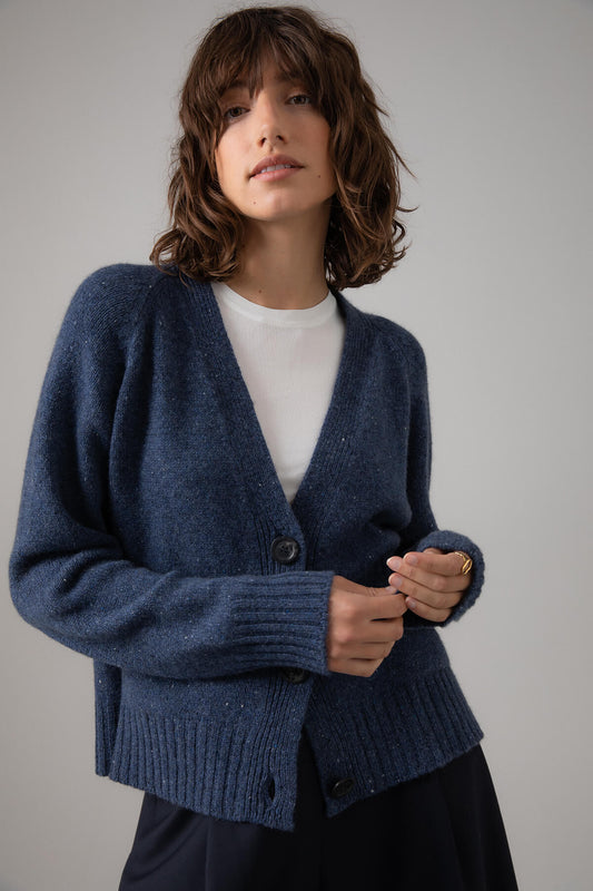 Johnstons of Elgin Women's Relaxed Fit V Neck Donegal Cashmere Cardigan in Denim Donegal  worn on a grey background KAC05090004383