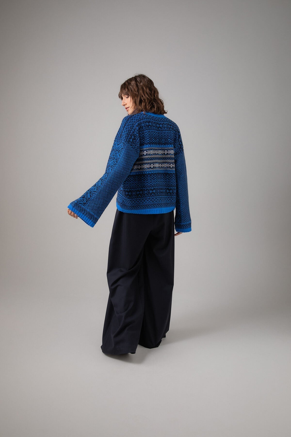 Back of Johnstons of Elgin Women's Round Neck Traditional Sanquhar Fairisle Cashmere Sweater in Orkney Blue worn with a Navy Trousers on a grey background KAC05099Q23725