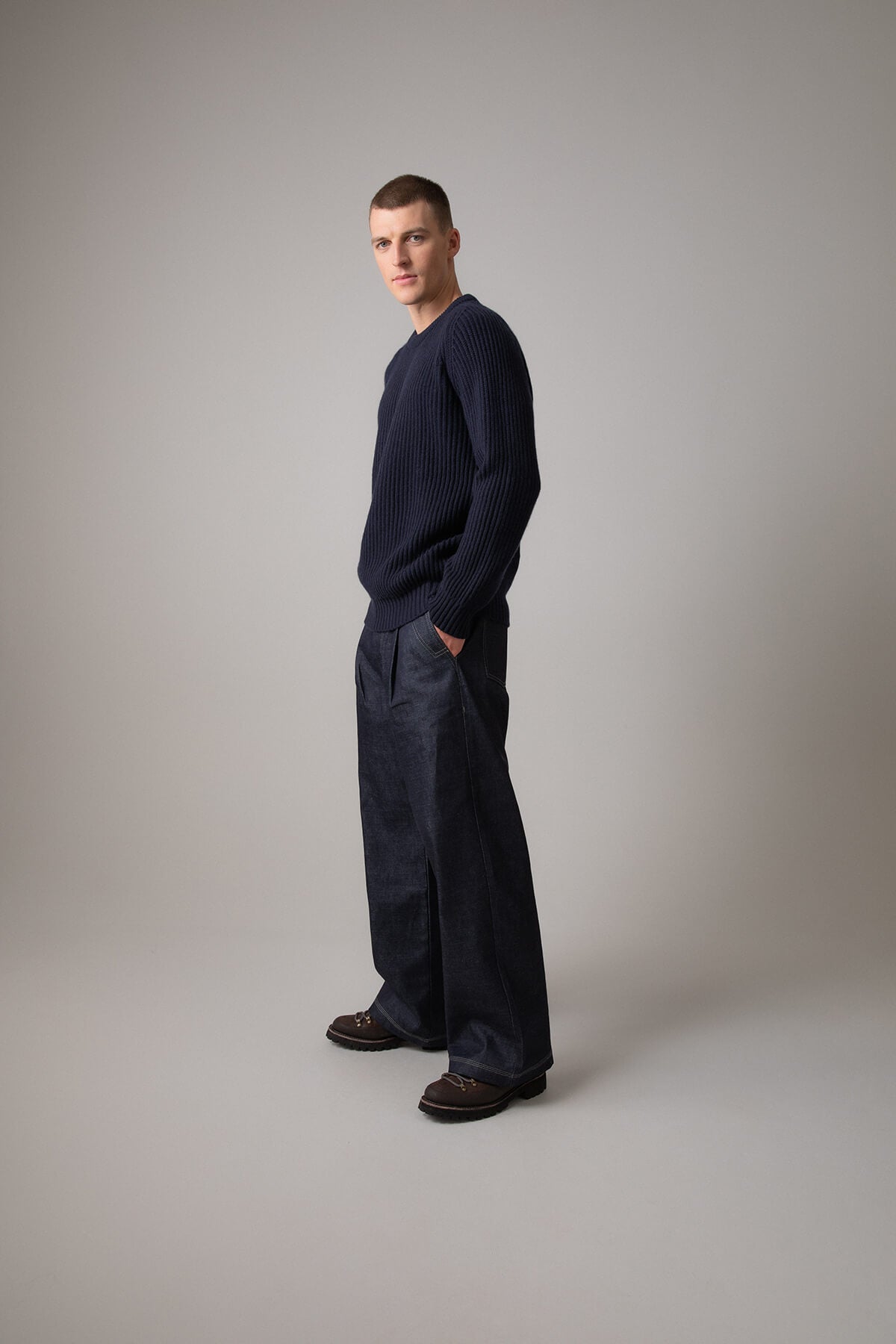 Johnstons of Elgin’s Men's Cashmere Ribbed Round Neck Jumper in Dark Navy on model wearing navy trousers on a grey background KAC05109SD7286