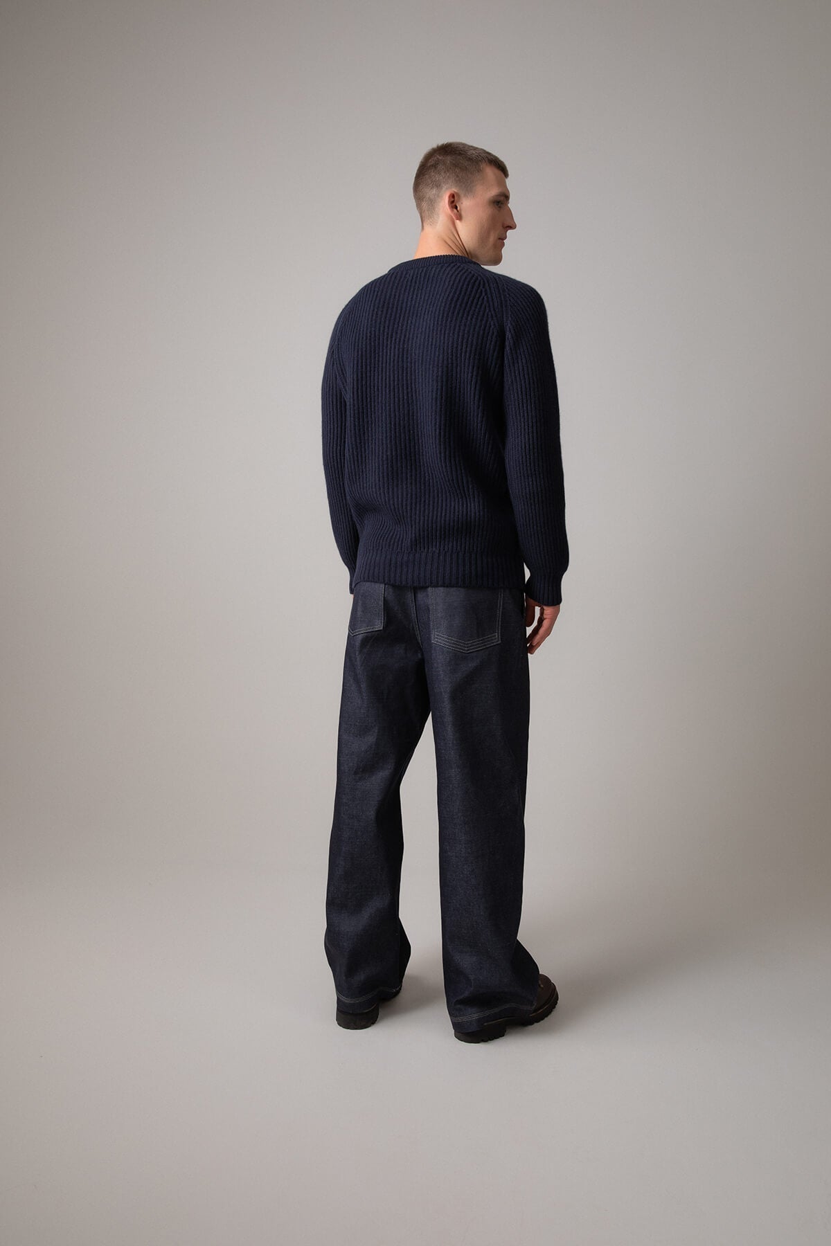 Johnstons of Elgin’s Men's Cashmere Ribbed Round Neck Jumper in Dark Navy on model wearing navy trousers on a grey background KAC05109SD7286