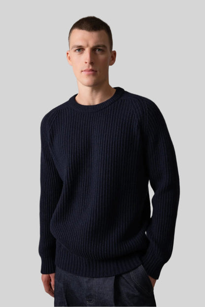 Johnstons of Elgin’s Men's Cashmere Ribbed Round Neck Jumper in Dark Navy on model wearing navy trousers on a grey background KAC05109SD7286