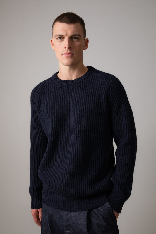 Johnstons of Elgin’s Men's Cashmere Ribbed Round Neck Jumper in Dark Navy on model wearing navy trousers on a grey background KAC05109SD7286