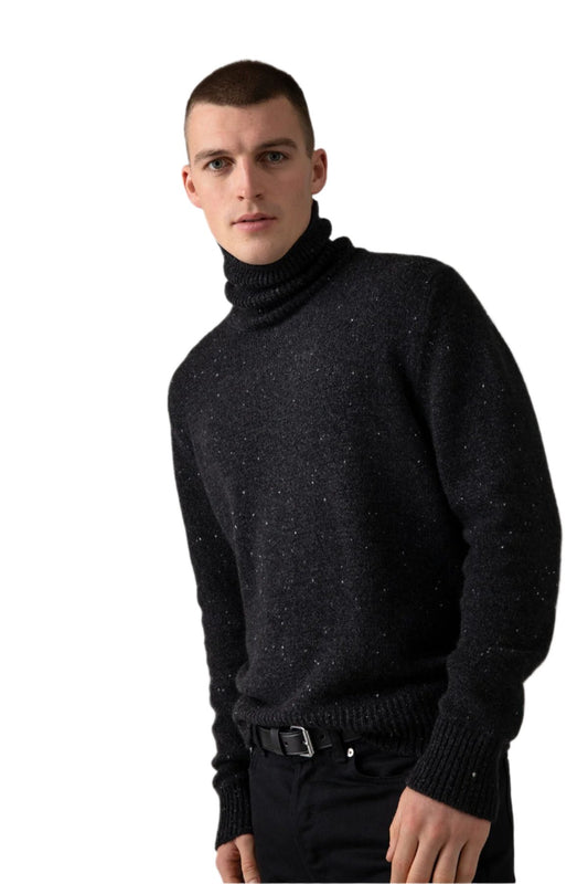 Johnstons of Elgin’s Men's Cashmere Donegal Roll Neck Jumper in Charcoal grey on model wearing black trousers on a grey background KAC05111002675