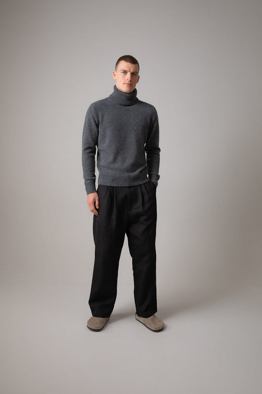 Johnstons of Elgin’s Men's Cashmere Donegal Roll Neck Jumper in Mid grey on model wearing black joggers on a grey background KAC05111004506