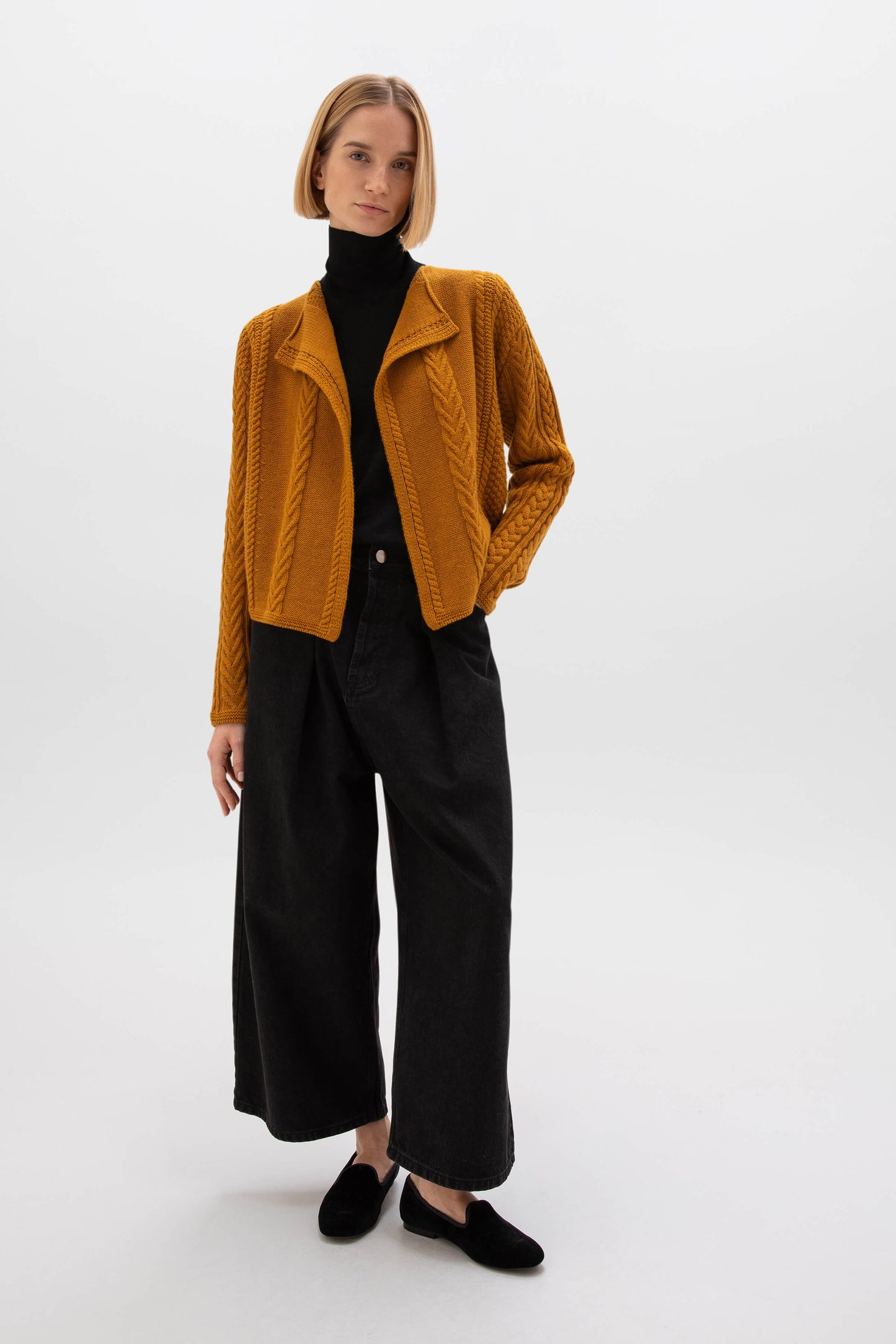 Woman wearing a mustard yellow cable knit jacket over a black turtleneck and wide-leg pants on a white background KAC05307SF4347