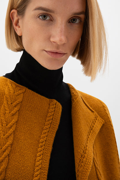 Person wearing a mustard yellow knitted cardigan over a black turtleneck on a white background KAC05307SF4347