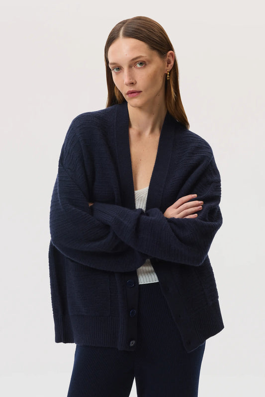 Female model Johnstons of Elgin SS25 Unisex Knitwear Navy Textured Cashmere Cardigan over a superfine white cashmere vest  KAC05415SD7286