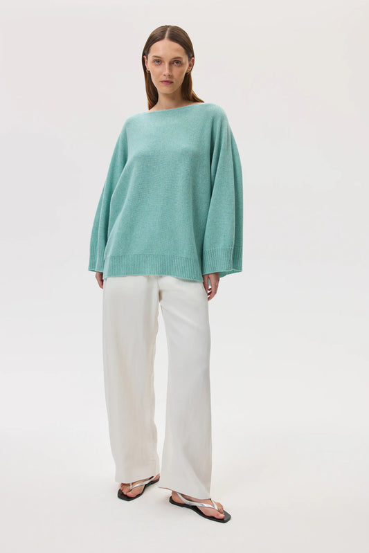 Model wearing Johnstons of Elgin SS25 Women's Knitwear Jade Cashmere Cape Jumper with white wide leg trousers KAI05048HC4284