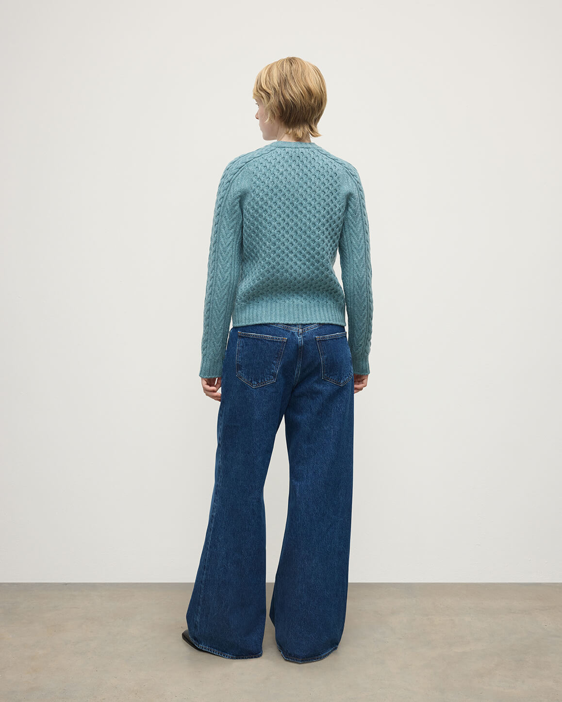 Model wears Johnstons of Elgin AW25 Women's Knitwear Seascape Aran Cable Green Cashmere Jumper Back View KAI05086HC0038