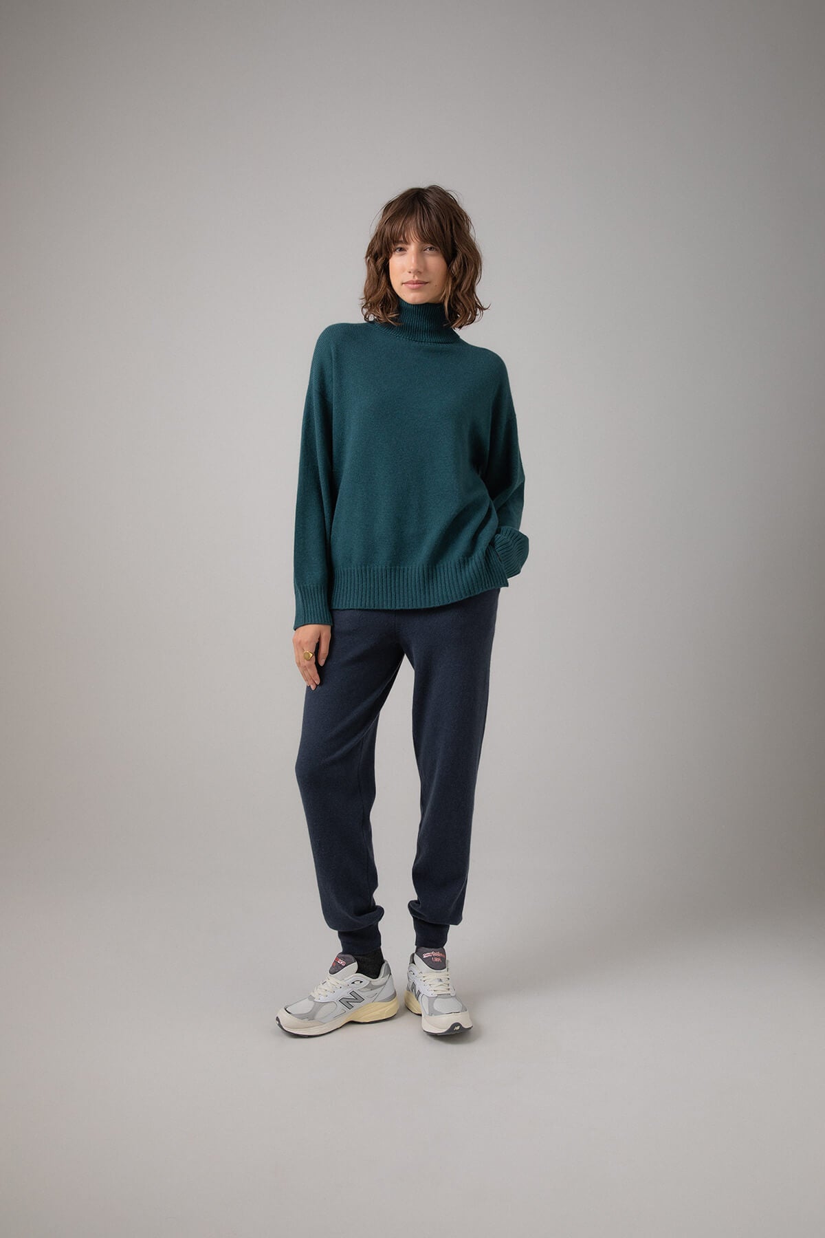 Johnstons of Elgin Women's Gauzy Cashmere Roll Neck with Stepped Hem in Mallard worn with Cashmere Joggers on a grey background KAI05100HC7126