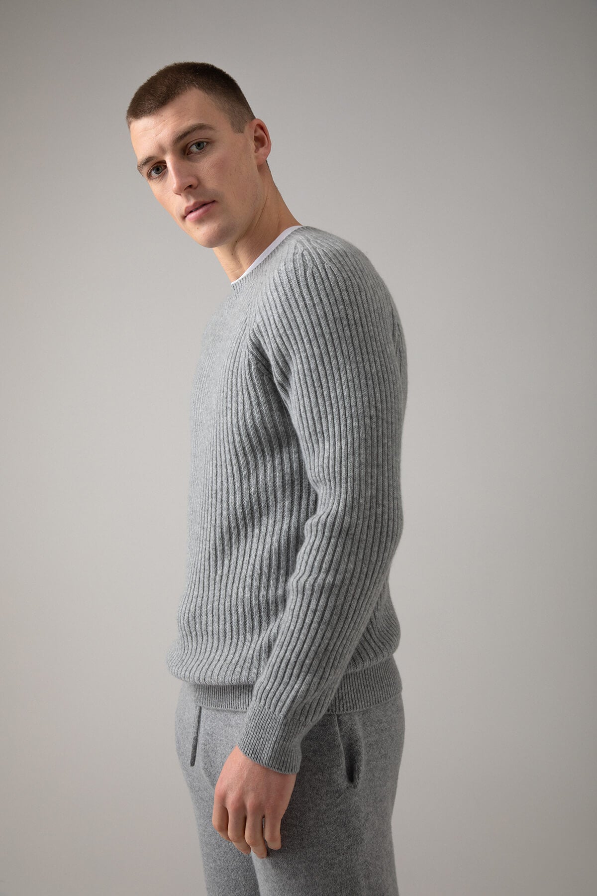 Johnstons of Elgin’s Men's Ribbed Cashmere Round Neck Jumper in Light Grey on model wearing grey joggers on a grey background KAI05105HA0308