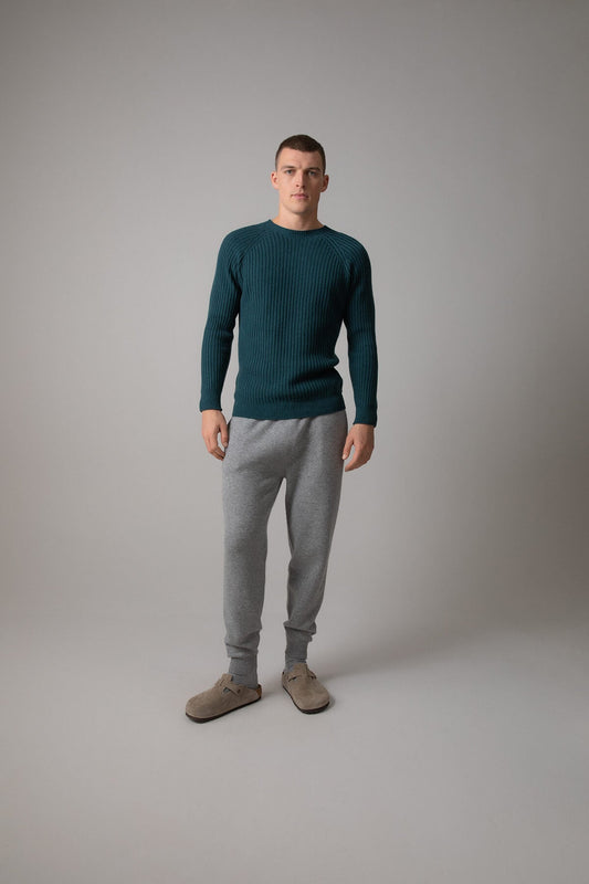 Johnstons of Elgin’s Men's Ribbed Cashmere Round Neck Jumper in mallard green on model wearing grey joggers on a grey background KAI05105HC7126