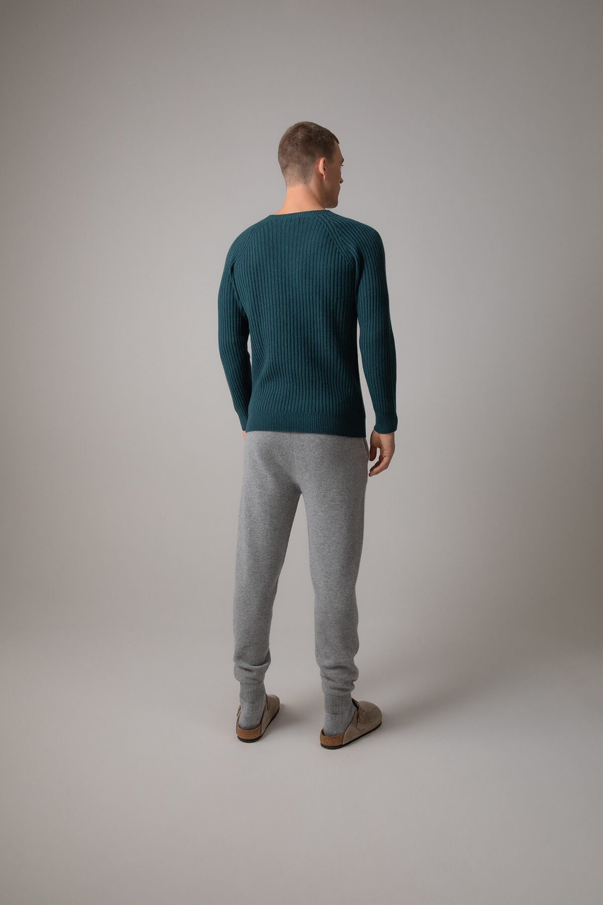 Johnstons of Elgin’s Men's Ribbed Cashmere Round Neck Jumper in mallard green on model wearing grey joggers on a grey background KAI05105HC7126