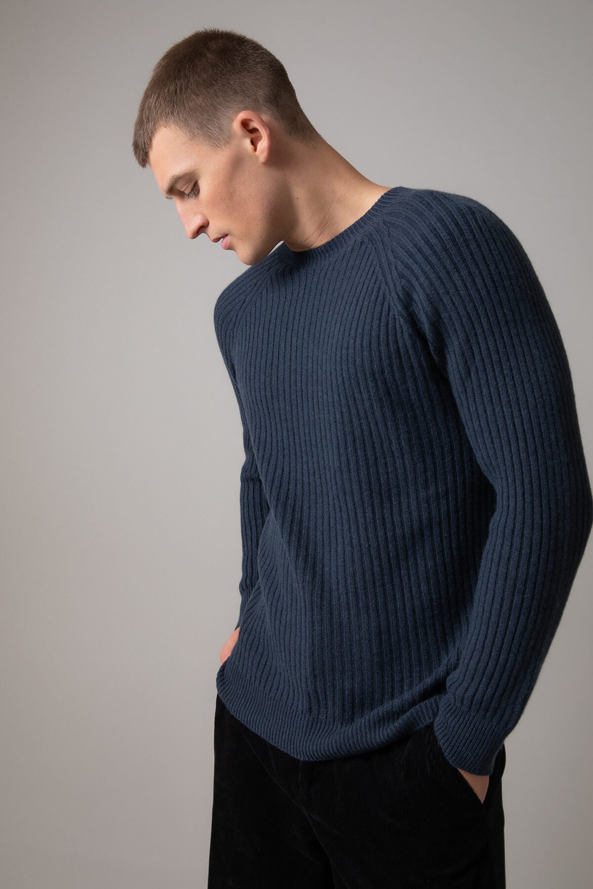 Johnstons of Elgin’s Men's Ribbed Cashmere Round Neck Jumper in Mazarine blue on model wearing black trousers on a grey background KAI05105SD7351