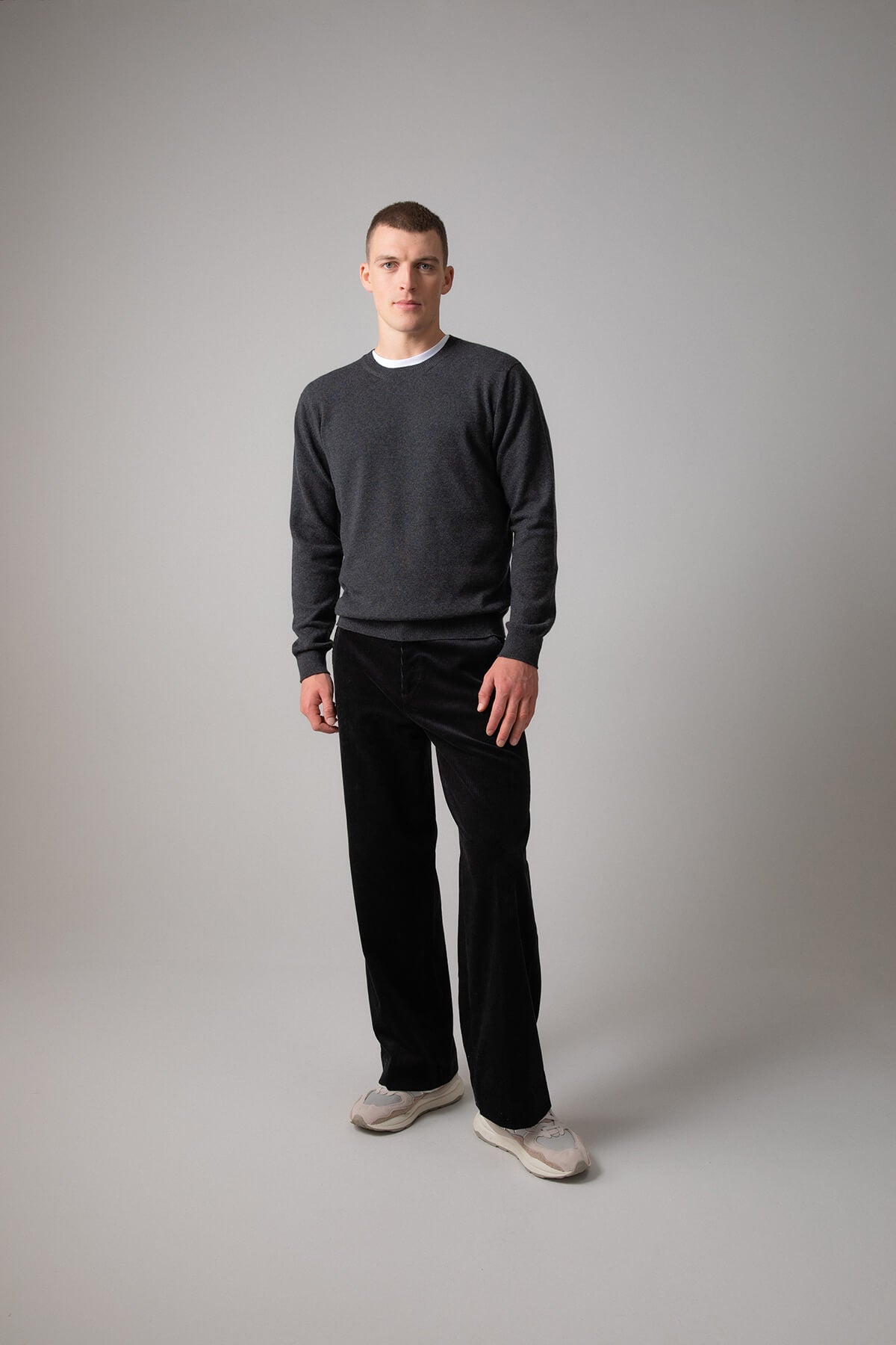 Johnstons of Elgin Men’s Cashmere Round Neck Jumper in Charcoal grey on model wearing black trousers on grey background KAI05117HA7165