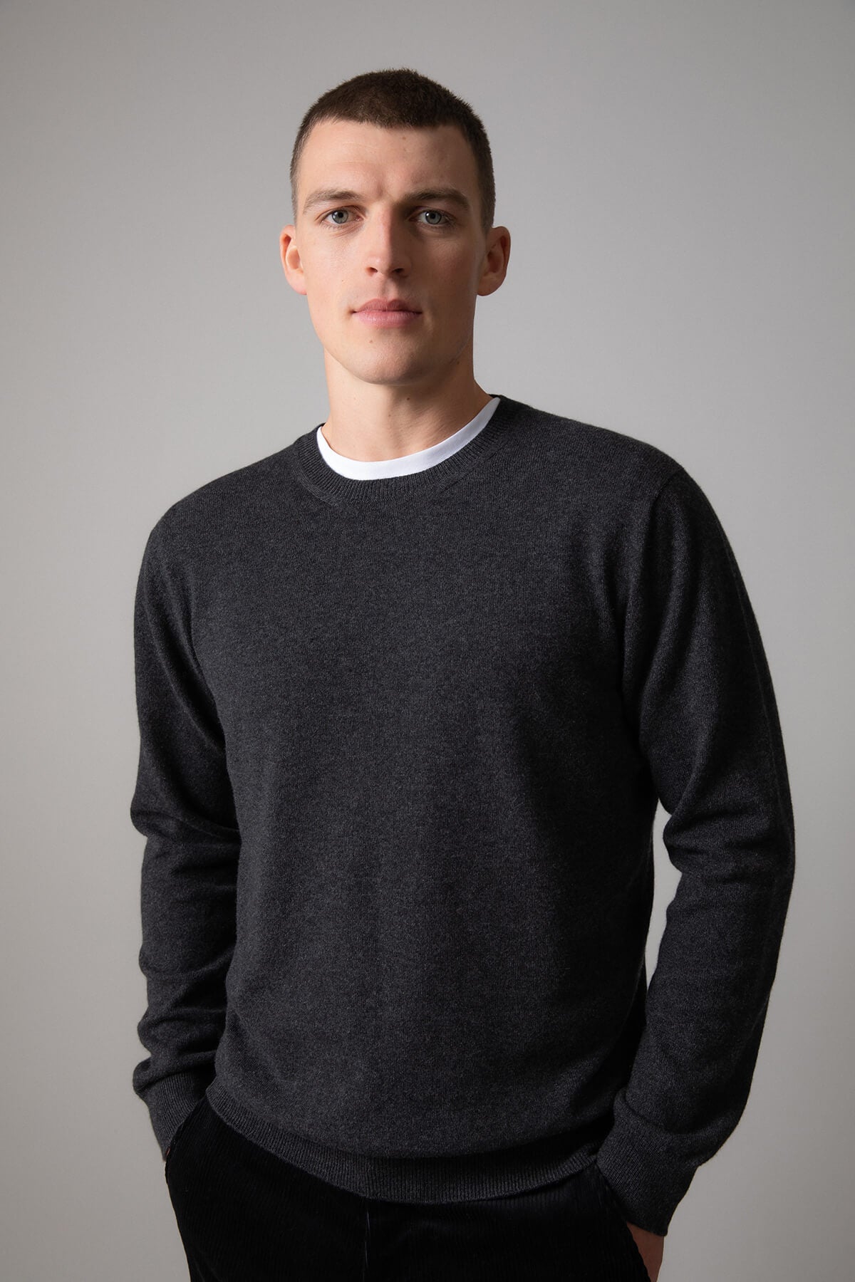 Johnstons of Elgin Men’s Cashmere Round Neck Jumper in Charcoal grey on model wearing black trousers on grey background KAI05117HA7165