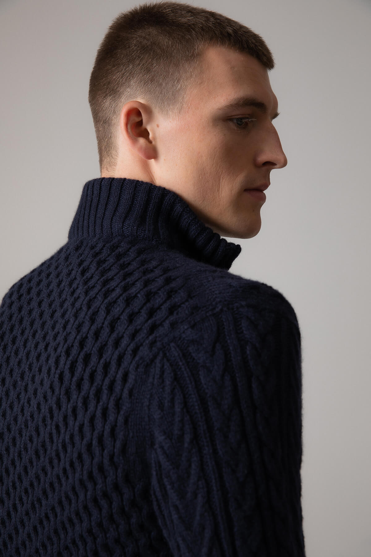 Johnstons of Elgin’s Men's Aran Cable Cashmere Zip Cardigan in Dark Navy on model on a grey background KAI05119Q23706