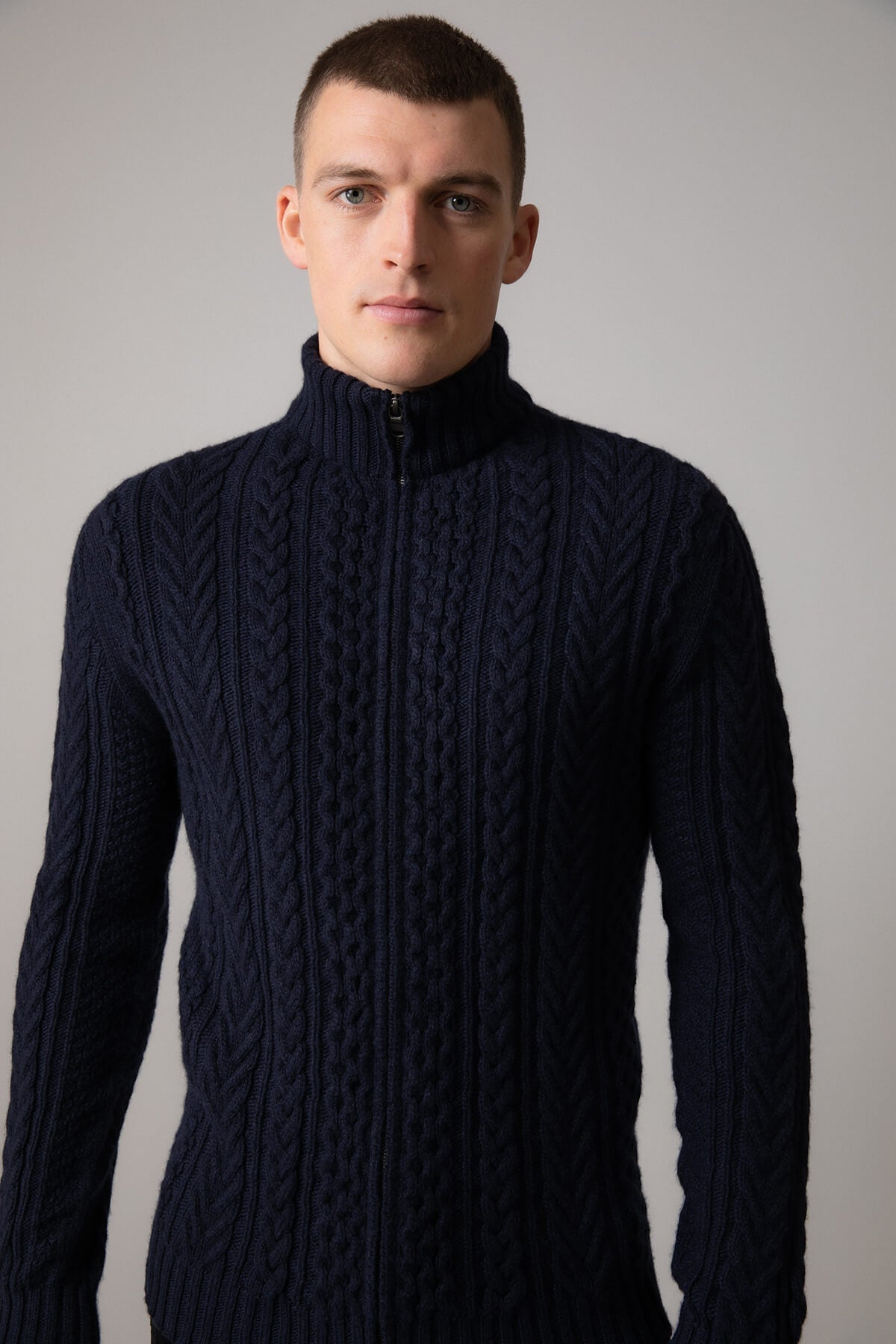 Johnstons of Elgin’s Men's Aran Cable Cashmere Zip Cardigan in Dark Navy on model on a grey background KAI05119Q23706