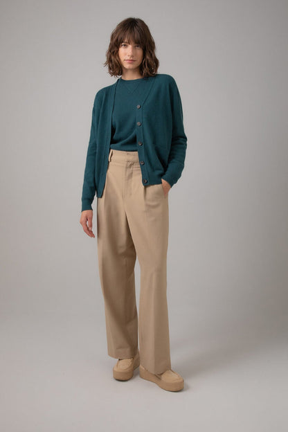 Johnstons of Elgin Women's Cashmere Boyfriend Cardigan in Mallard green worn with a matching Crew Neck and Beige Chinos on a grey background KAI05141HC7126
