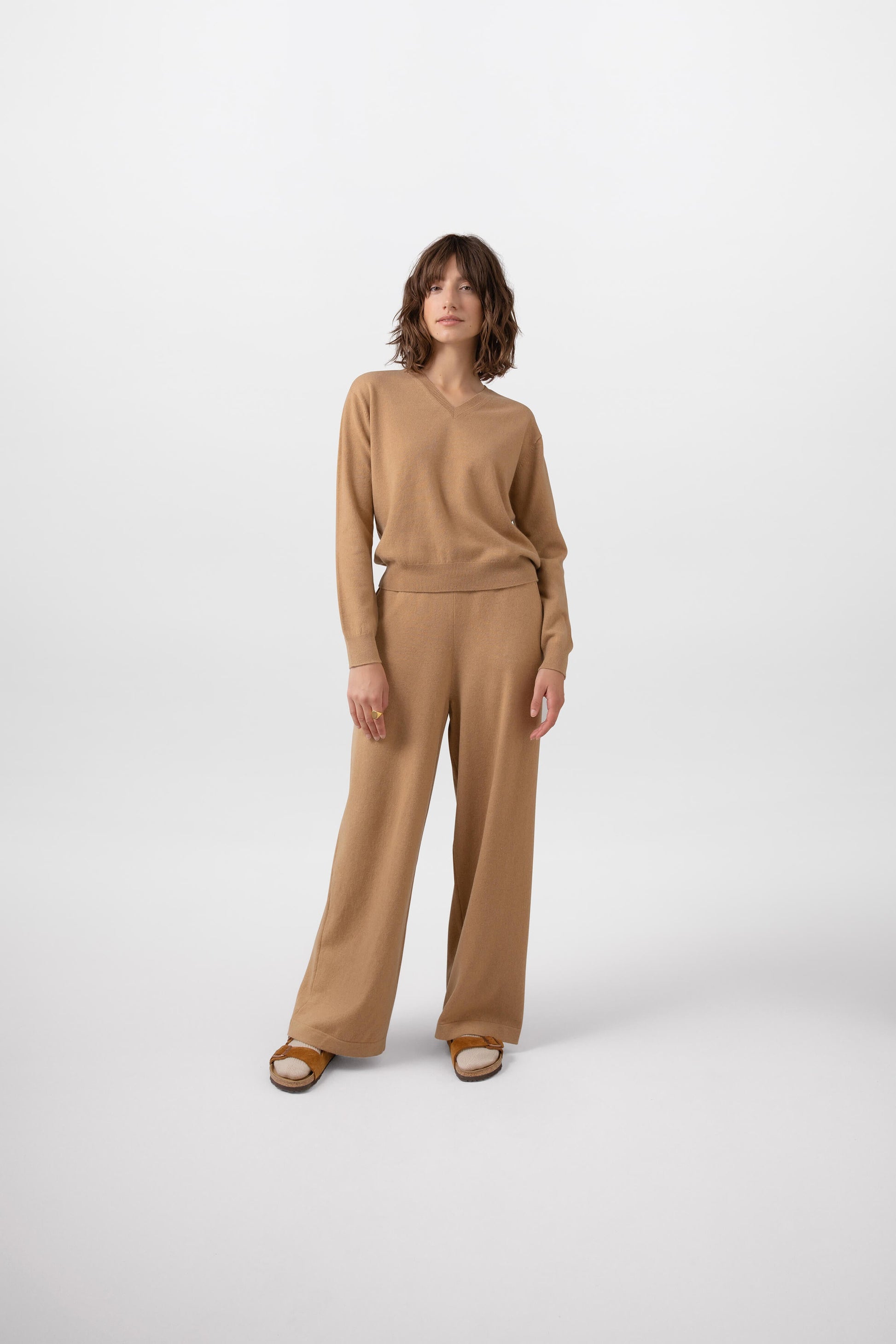 Johnstons of Elgin Knitted Cashmere Women's High Rise Wide Leg Trousers in Camel worn with a matching Cashmere Sweater on a grey background KBP00926HB4315