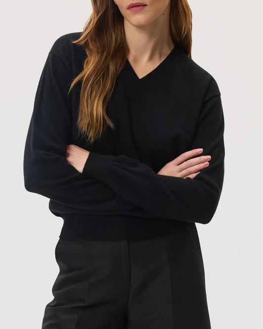 Model wears Johnstons of Elgin SS25 Women's Knitwear Black Classic Cashmere V Neck Jumper with black knee length shorts KAI05143SA0900